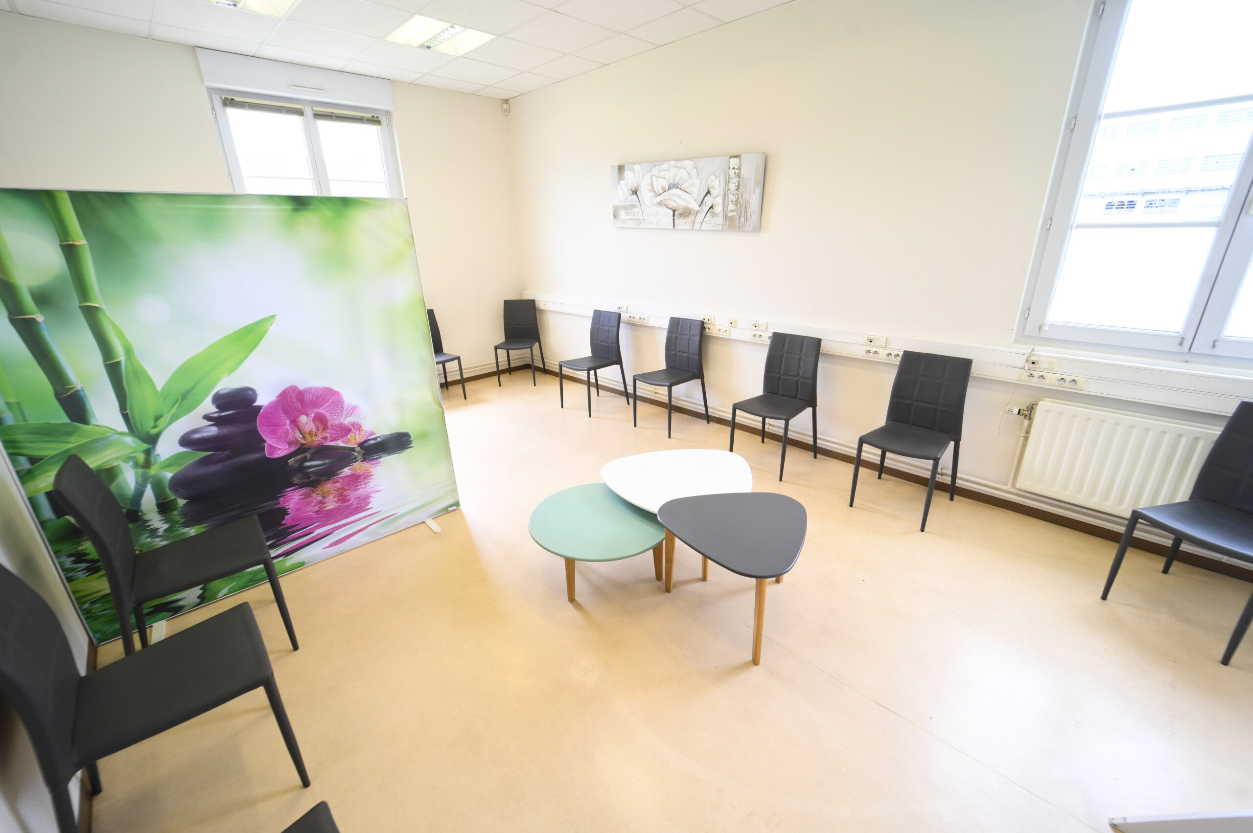 Une salle d'attente moderne avec une décoration murale florale, plusieurs chaises alignées contre le mur et deux tables basses ovales au centre du Laboratoire Givet Bio Ard'Aisne.