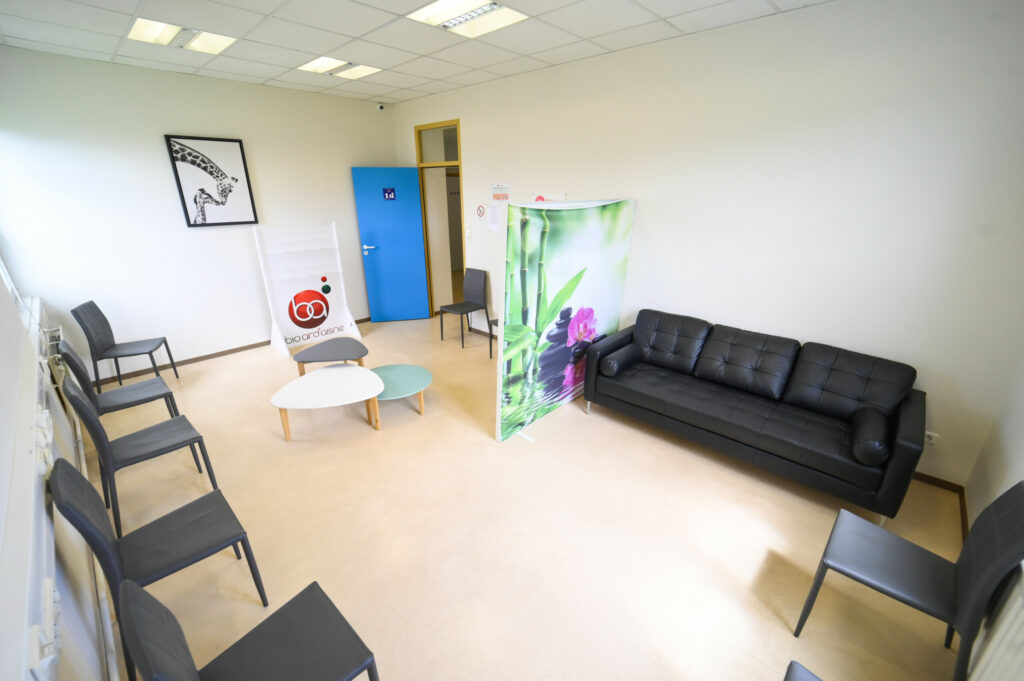 Intérieur d'une salle d'attente moderne du Laboratoire Givet Bio Ard'Aisne avec canapé noir, chaises, banderoles décoratives et œuvres d'art sur les murs.