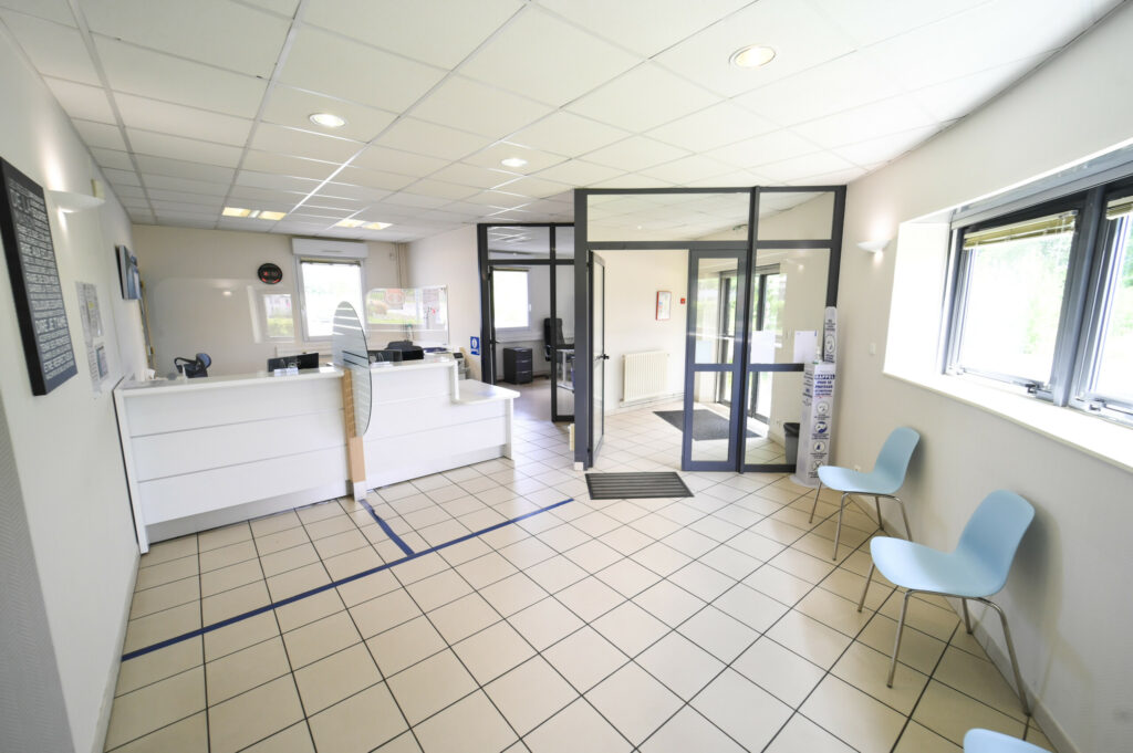 Espace de réception bien éclairé du Laboratoire Givet Bio Ard'Aisne avec comptoirs blancs, chaises bleues, carrelage au sol et affiches d'information aux murs.