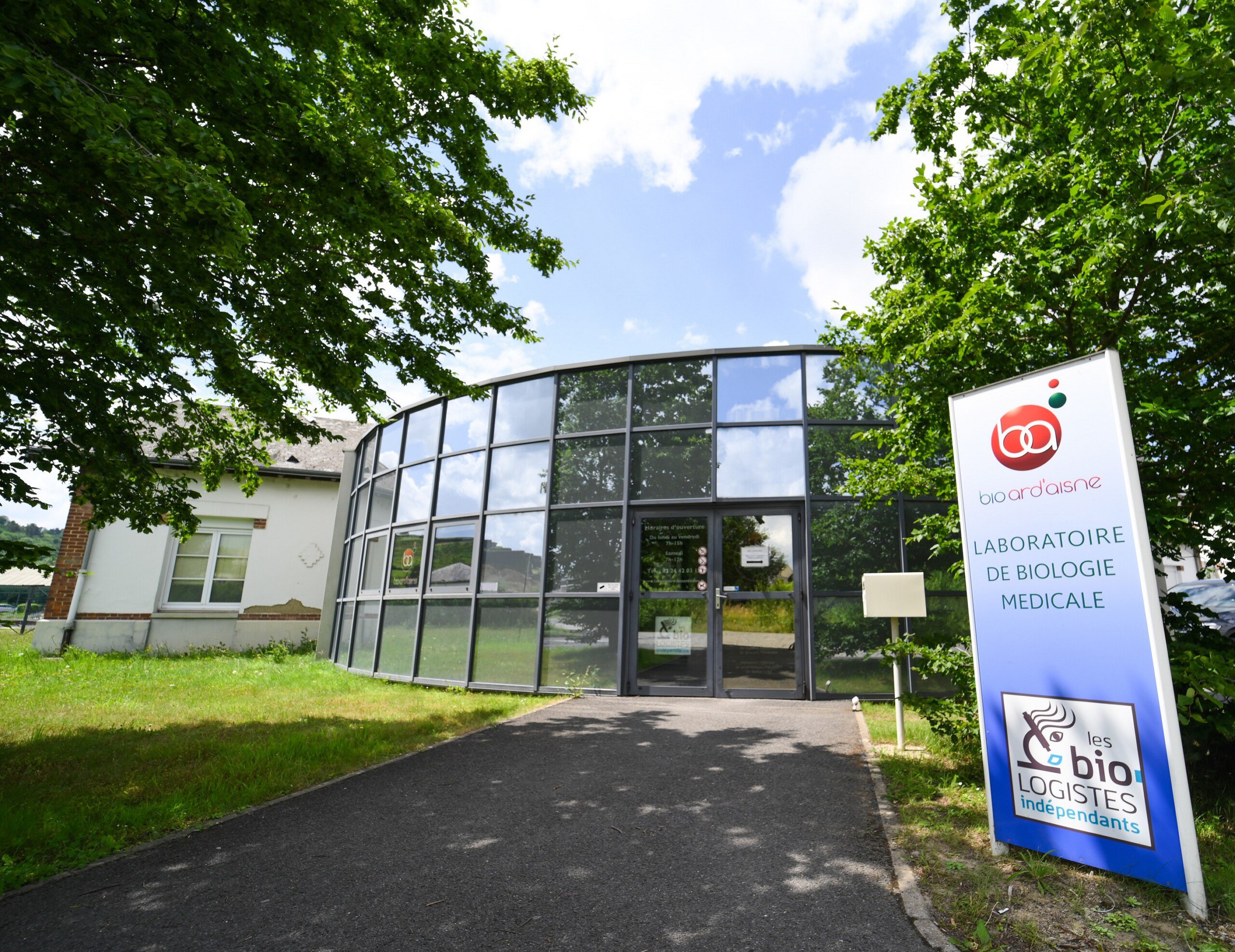Vue extérieure d'un laboratoire médical avec une façade vitrée courbée et des panneaux indiquant "Laboratoire Givet Bio Ard'Aisne".