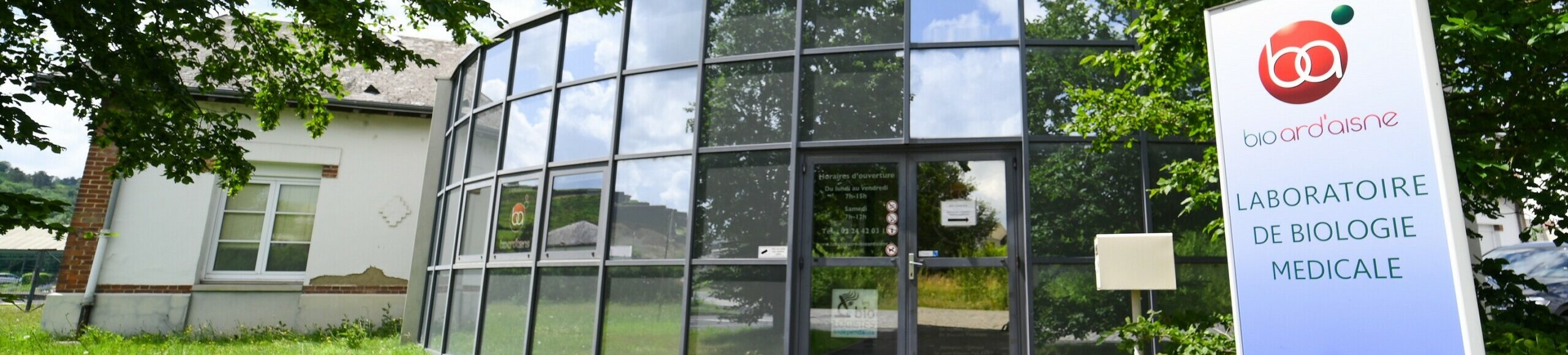 Vue extérieure d'un bâtiment de laboratoire médical avec une grande façade vitrée et une enseigne portant le logo "Laboratoire Givet Bio Ard'Aisne".