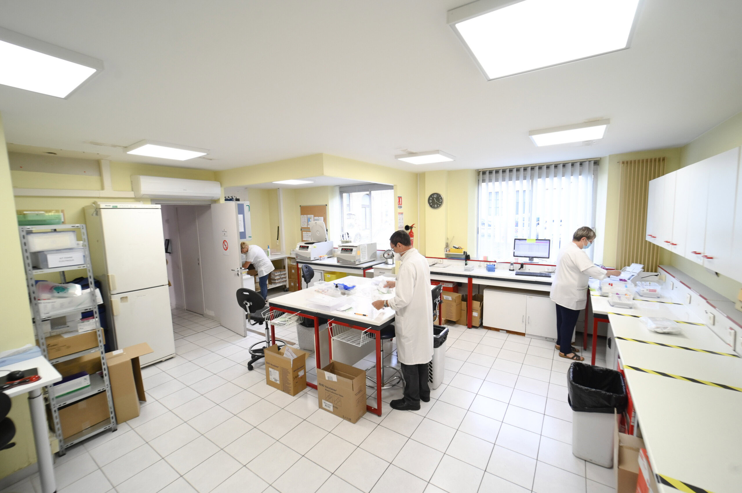 Trois techniciens de laboratoire en blouse blanche travaillant dans le Laboratoire Sedan La Marck, lumineux et moderne, doté de divers équipements médicaux.