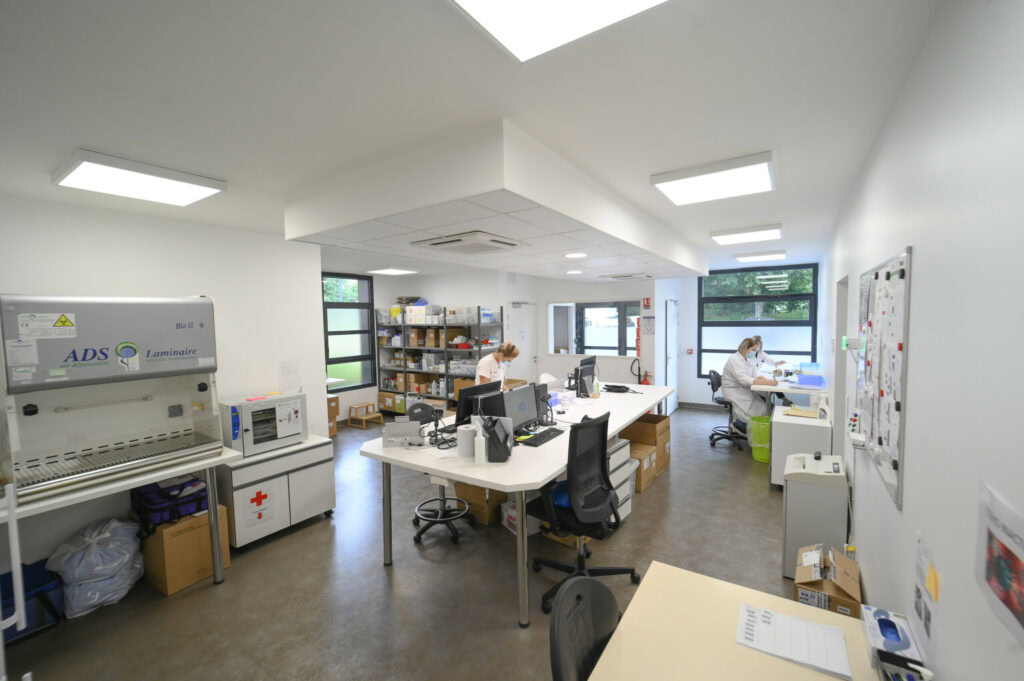 Intérieur du Laboratoire Balan Bio Ard'Aisne avec plusieurs techniciens travaillant à des bureaux et utilisant des équipements électroniques, entourés de matériel médical dans une pièce lumineuse et bien éclairée.
