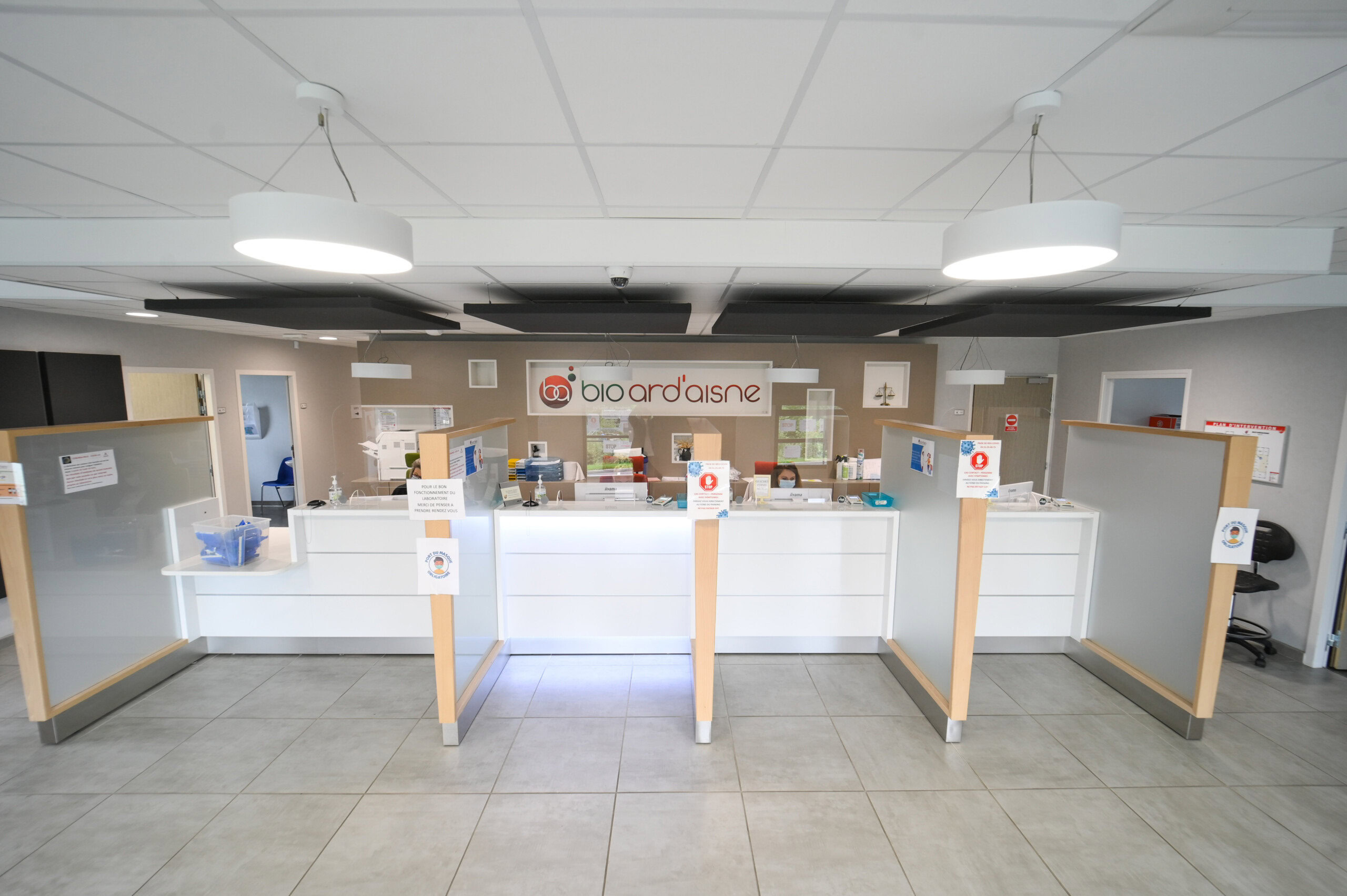 Un intérieur de pharmacie moderne avec un comptoir blanc, des écrans de protection et une signalétique favorisant la santé et le bien-être au Laboratoire Balan Bio Ard'Aisne.