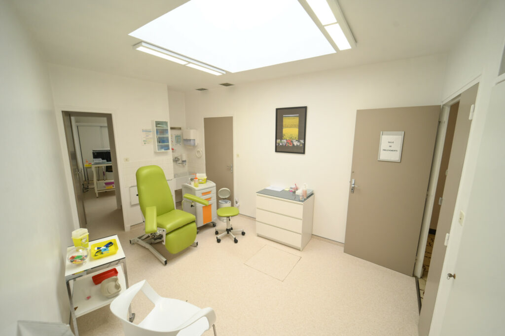 Salle d'examen médical lumineuse et spacieuse avec chaise verte, bureau, matériel du Laboratoire Vouziers Bio Ard'Aisne et puits de lumière.