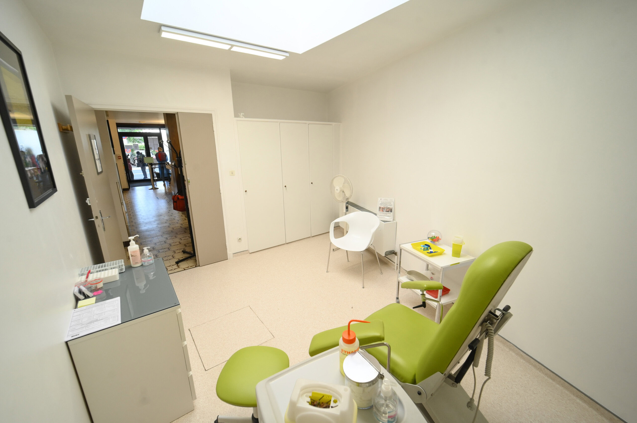 Une salle médicale lumineuse avec un fauteuil d'examen vert, des armoires blanches et du matériel médical du Laboratoire Vouziers Bio Ard'Aisne, menant à une porte ouverte.