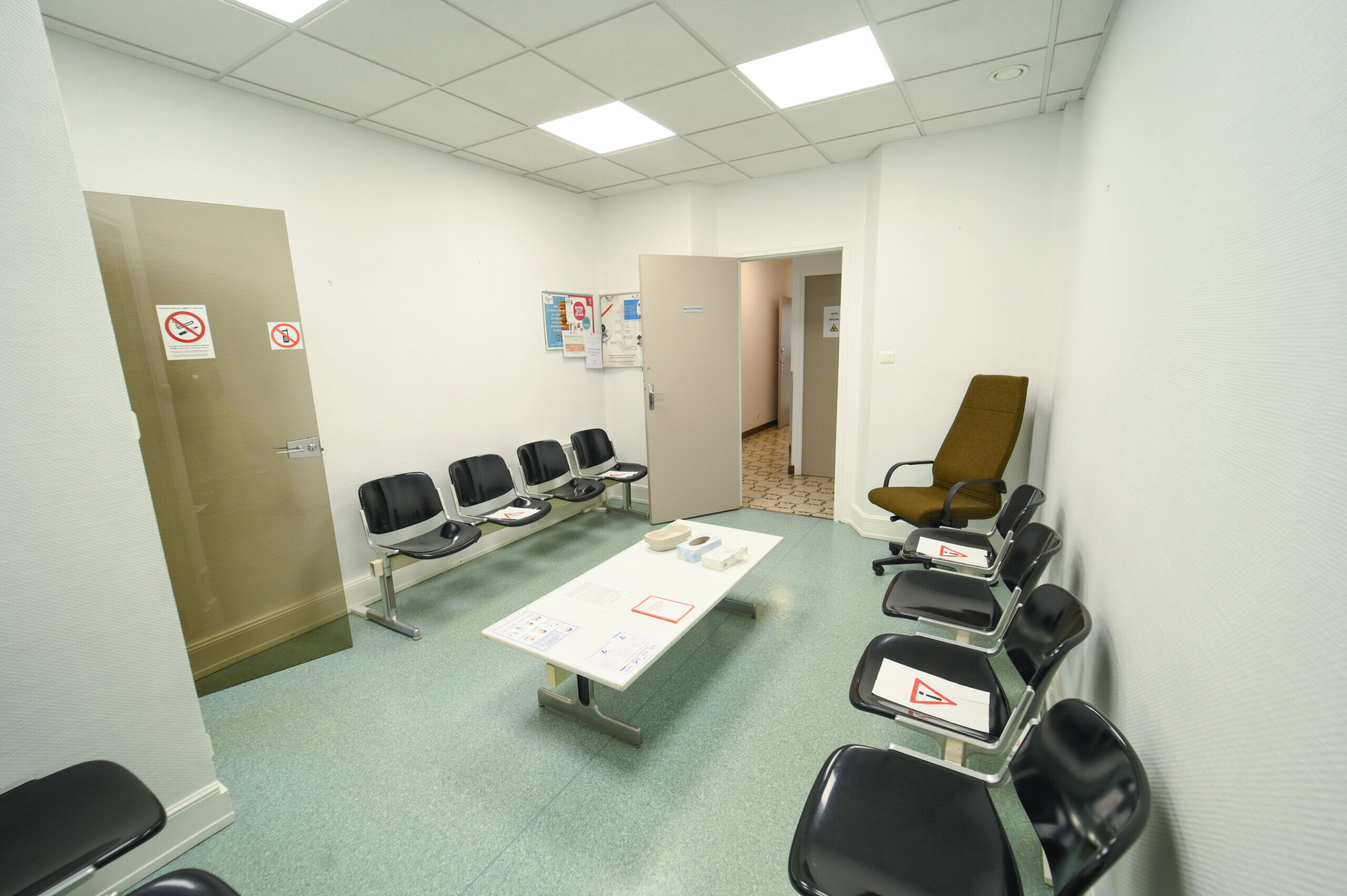 Intérieur d'une petite salle d'attente vide avec des rangées de chaises, des panneaux interdisant de fumer et des affiches d'information sur les murs blancs du Laboratoire Vouziers Bio Ard'Aisne.