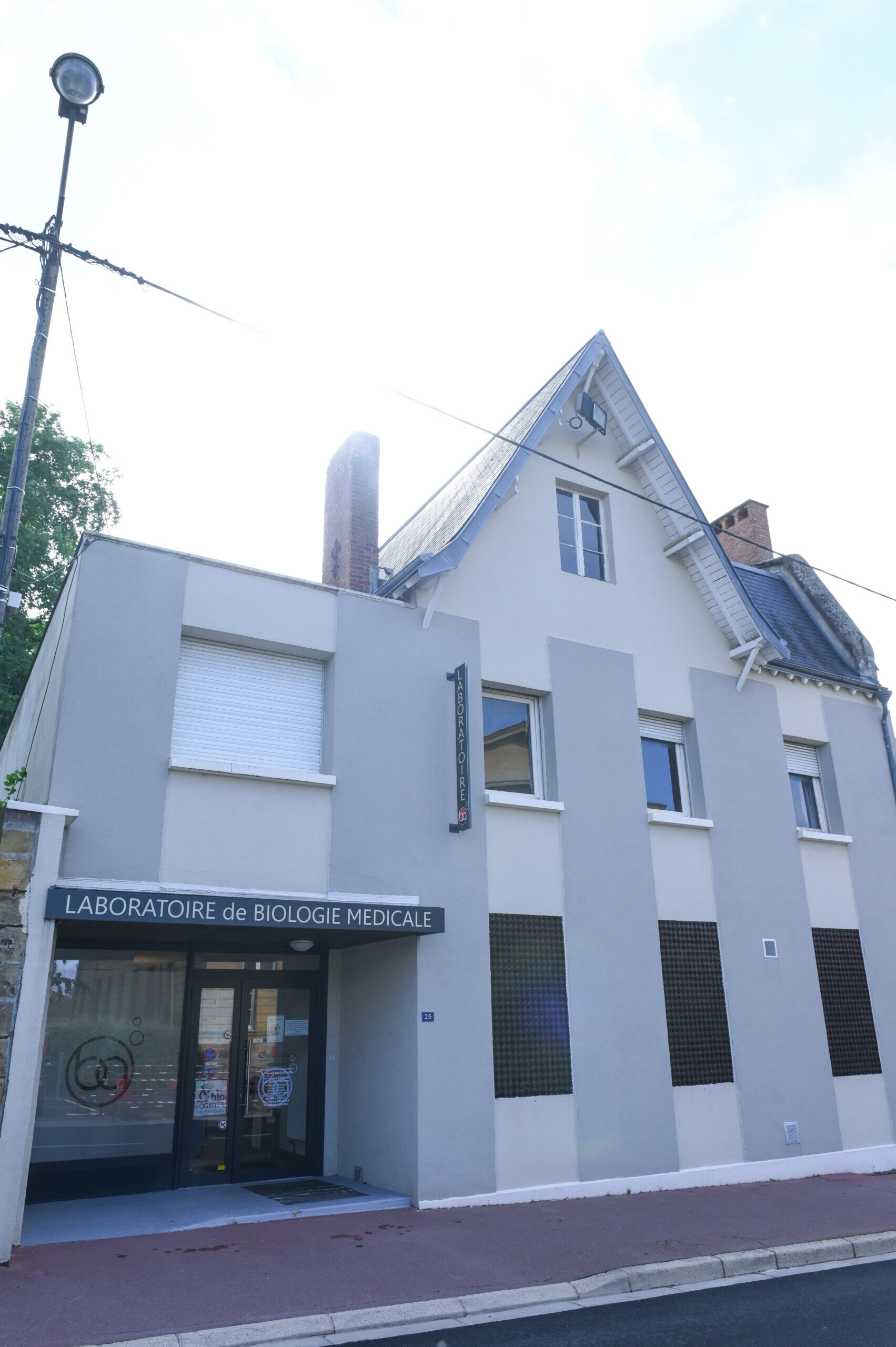 Vue extérieure du Laboratoire Vouziers Bio Ard'Aisne, un laboratoire médical sur deux étages avec une façade moderne et une architecture supérieure traditionnelle, situé au coin d'une rue ensoleillée.