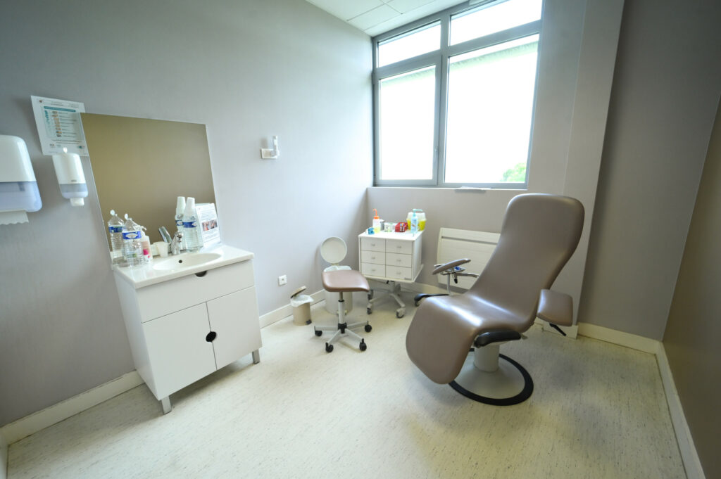 Une salle d'examen médical propre et moderne du Laboratoire Rethel Bio Ard'Aisne avec un fauteuil inclinable, un bureau, des fournitures et une fenêtre.