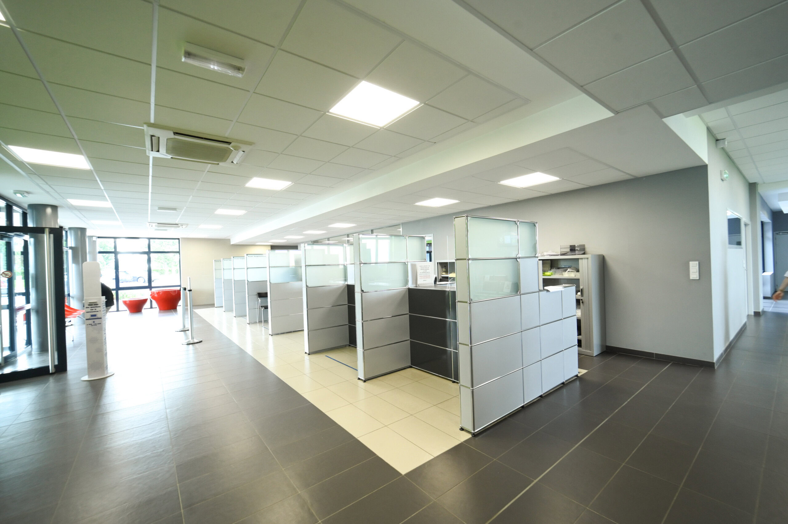 Espace d'accueil moderne avec guichets séparés, plafonniers lumineux, carrelage au sol et salle d'attente près de l'entrée du Laboratoire Rethel Bio Ard'Aisne.
